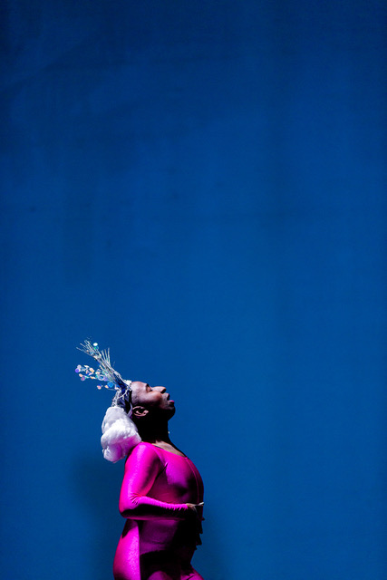 man in pink bodysuit and blue crown against a dark blue background