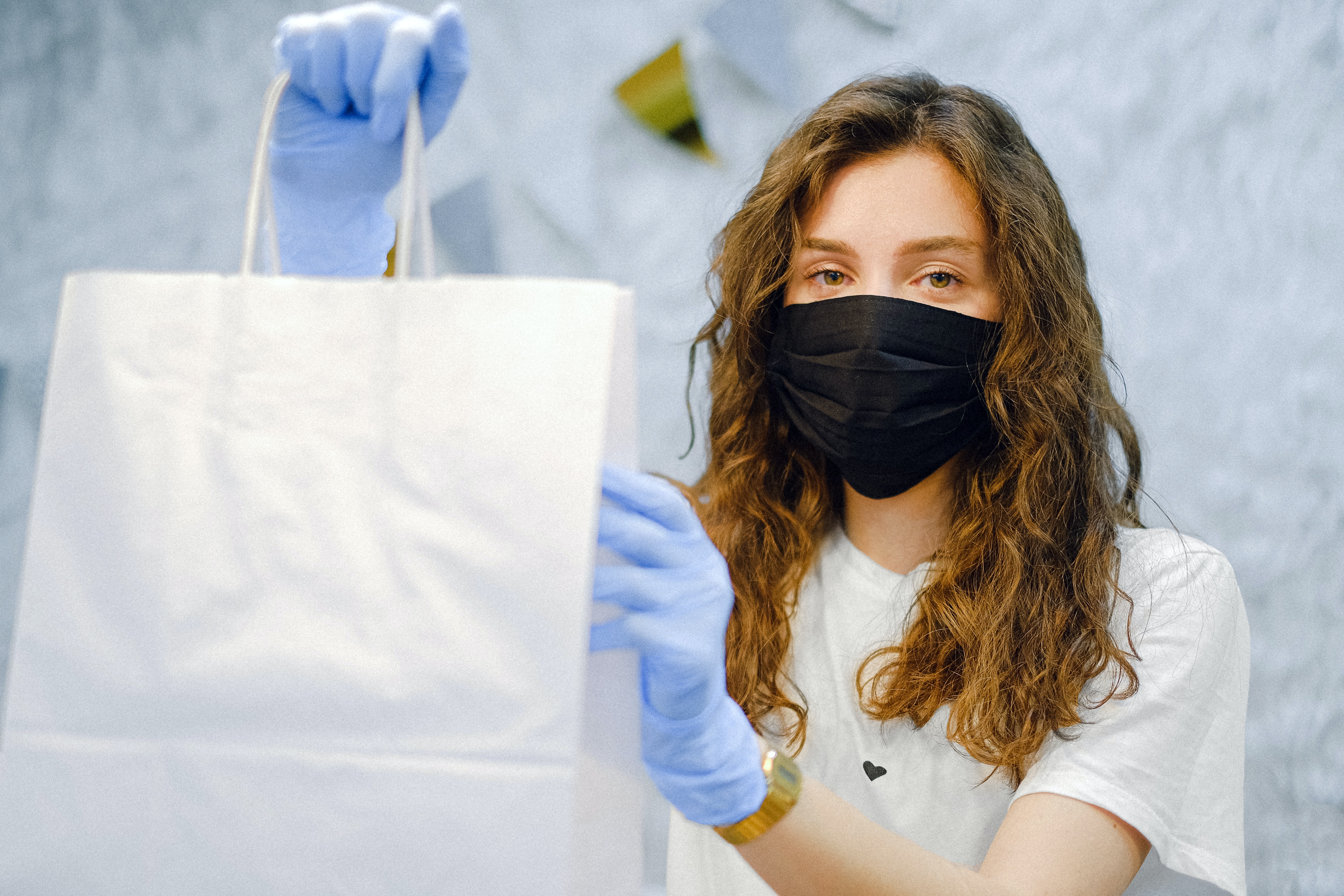 Woman in a black mask wearing gloves holding up a white shopping bag
