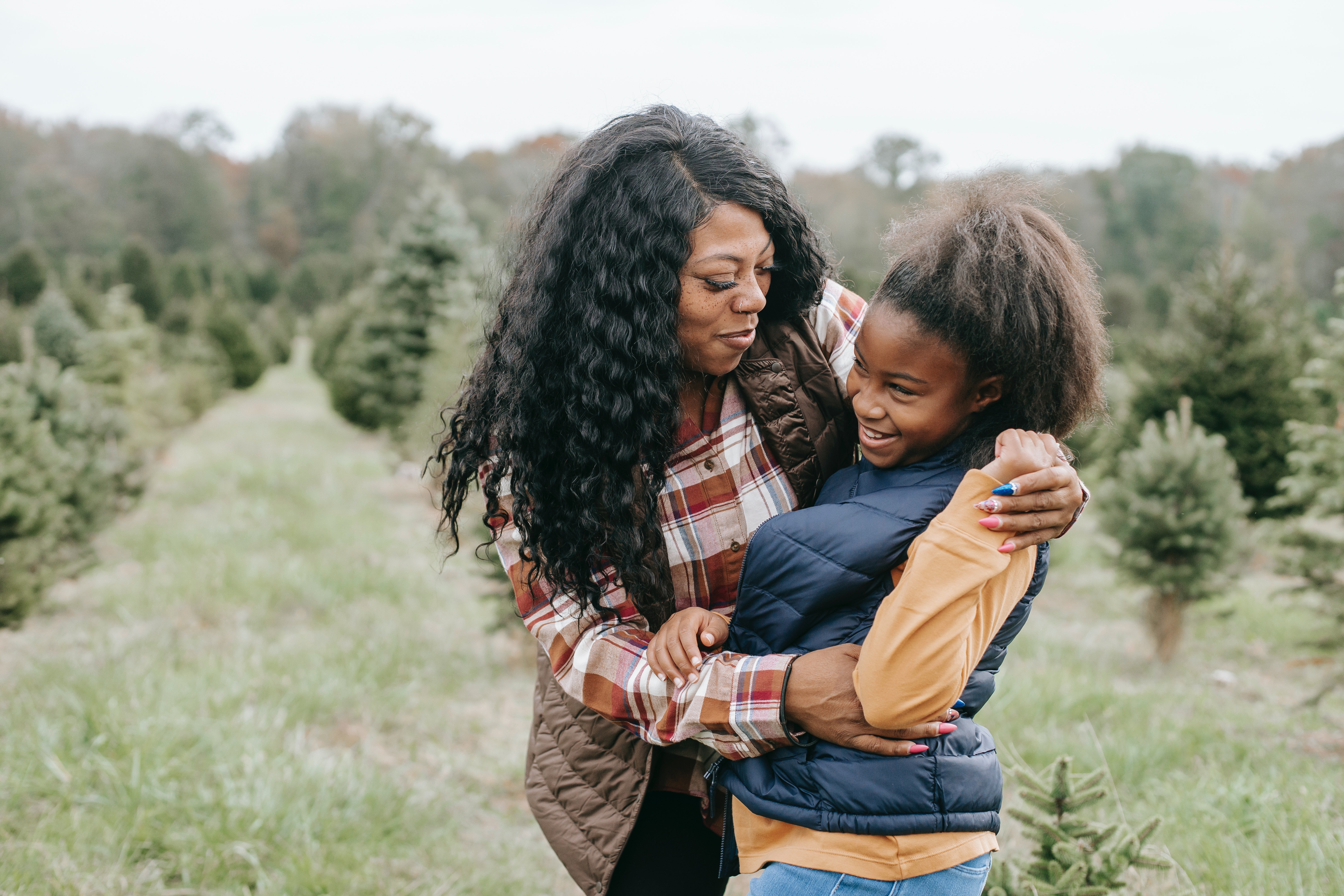 A woman hugging her daughter in a Christmas tree farm