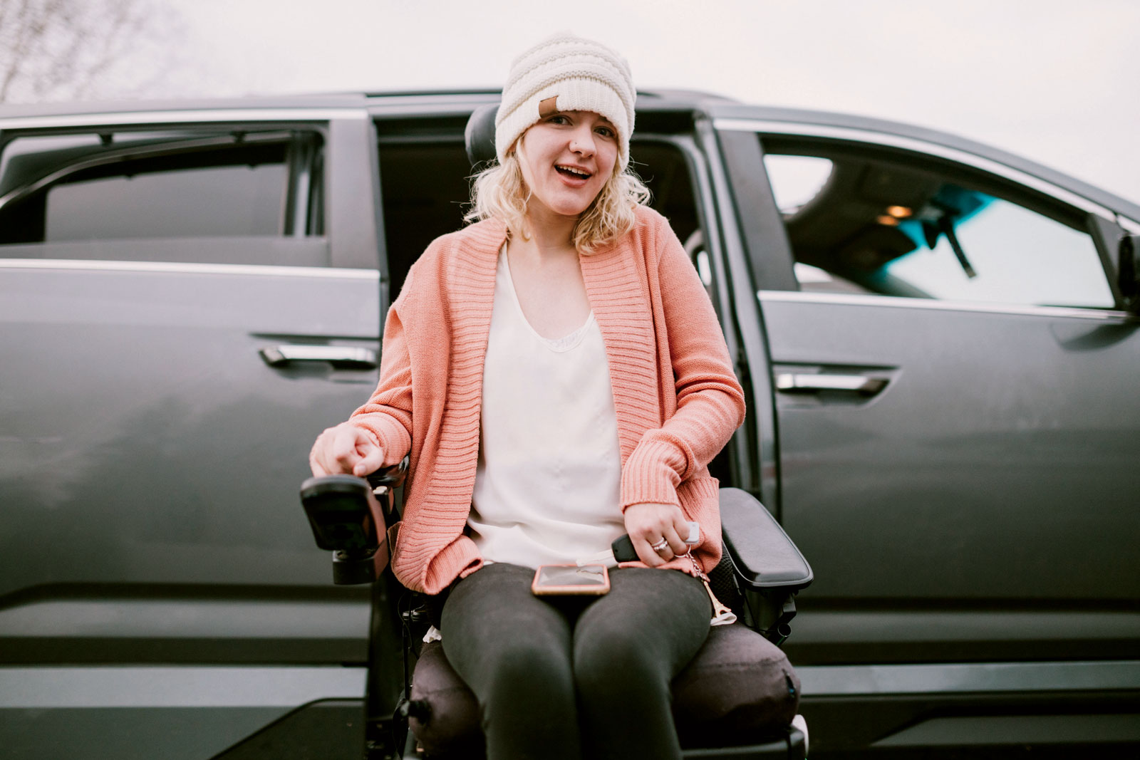 Woman in a automated wheelchair in a pink sweater outside of a silver car