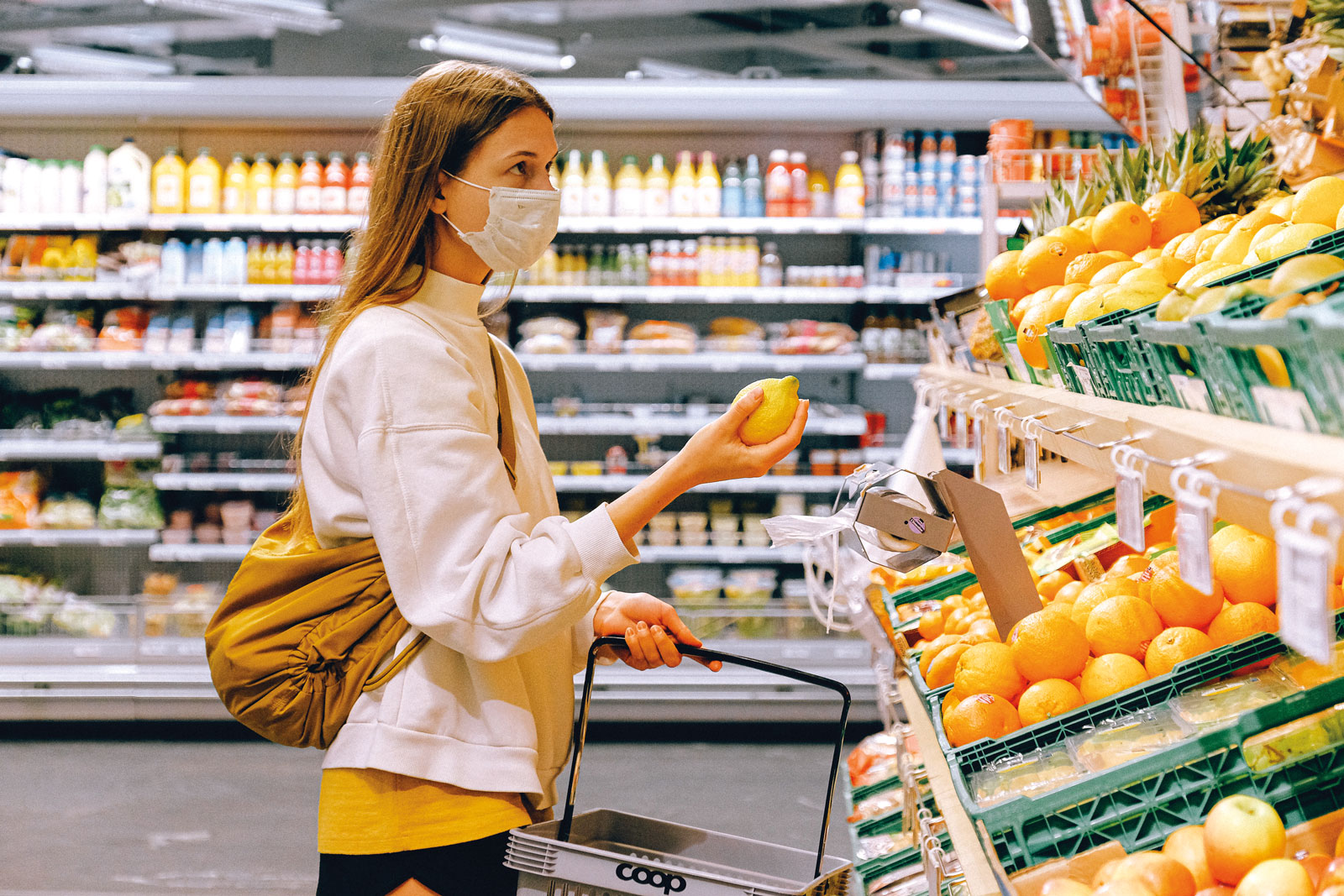 woman shopping in a grocery store for a lemon with a white mask