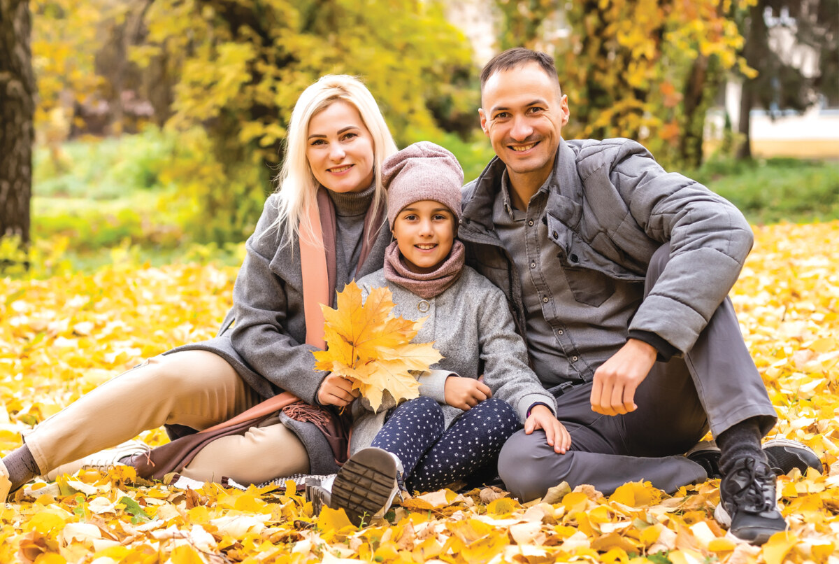 a family consisting of a mother, father, and young child sit in the leaves outside.