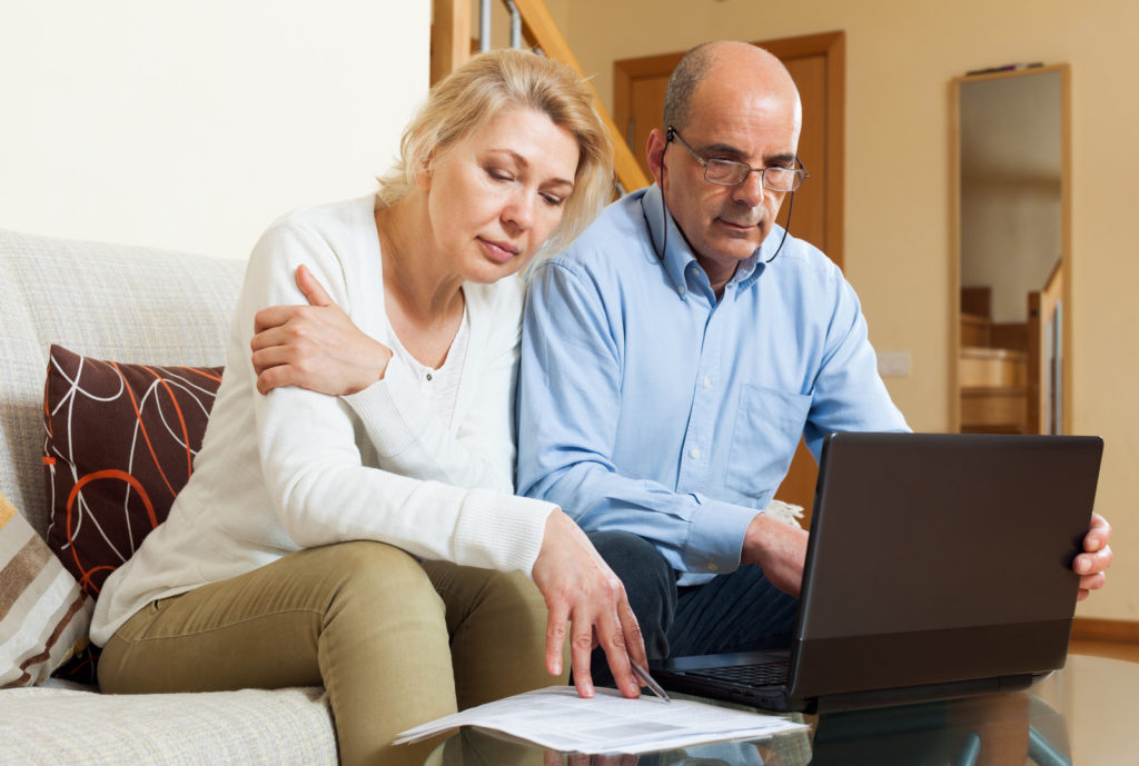 Man and woman sitting on a couch looking at a computer and a paper contract