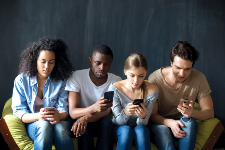 group of young adults sitting on a yellow couch on their cell phones