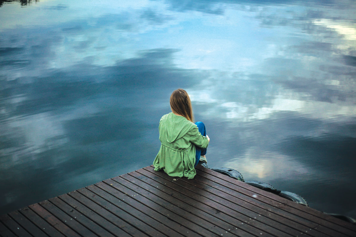 Woman sitting in front of a lake on a dock