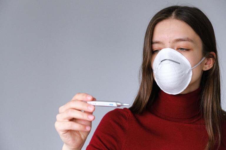 woman in a white mask and red shirt looking at a thermometer