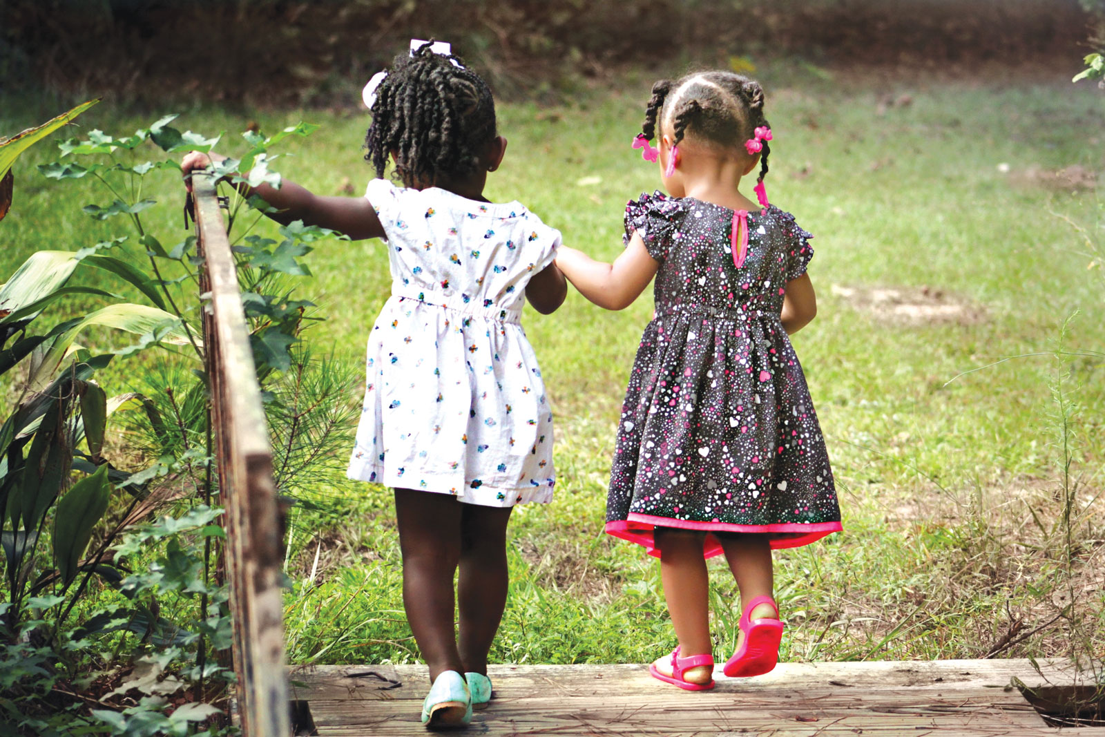 two little girls walking on a bridge in a garden