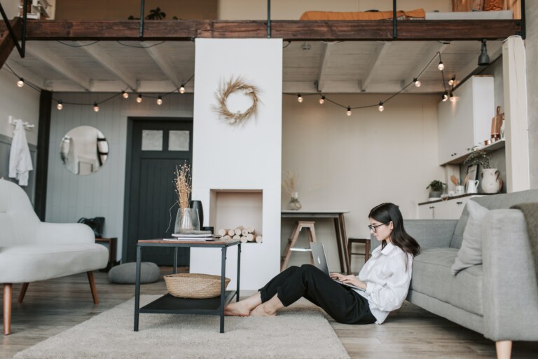 woman sitting in her living room on her computer with a large white wall in the background