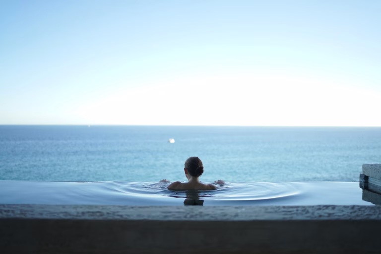 A woman sits in an infinity pool looking out over a large body of water.