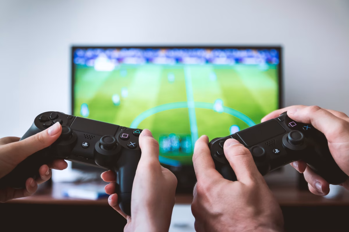 two people hold playstation controllers in their hands while facing a television with a soccer video game on it.