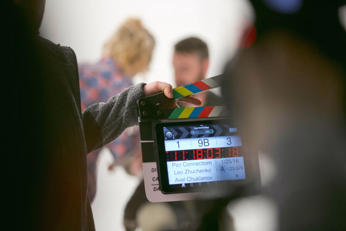 A man and a woman get ready to act on a film production set, with the foreground featuring a digital clapperboard used to synchronize audio and video during filming.