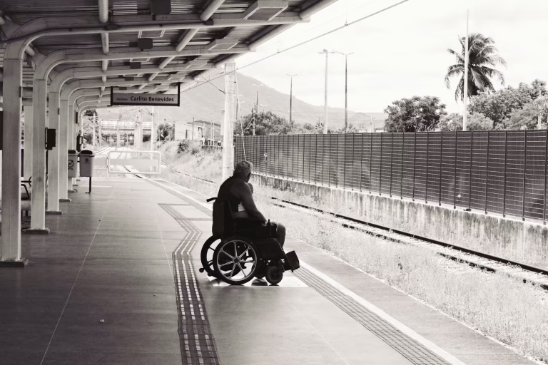 A man in a wheelchair waits on an empty outdoor train platform.