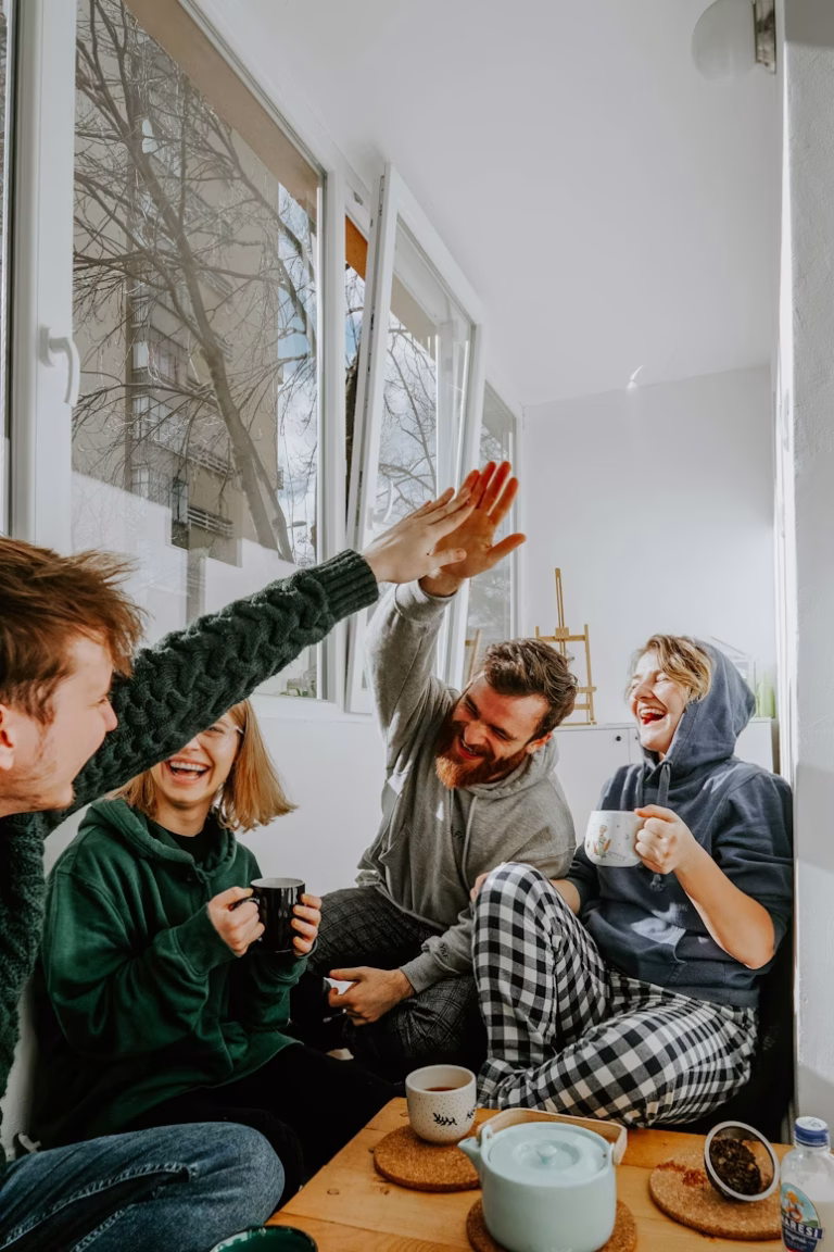 four friends sit at a coffee table laughing and drinking coffee.