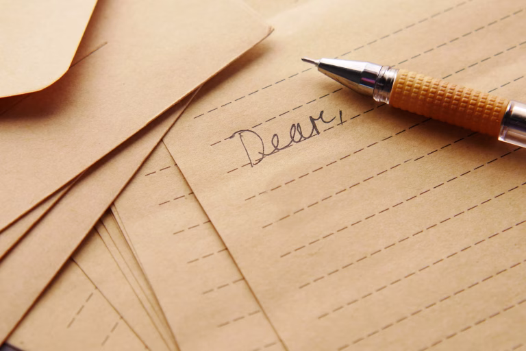 a stack of papers with a pen on the top. the word Dear is handwritten on the top paper
