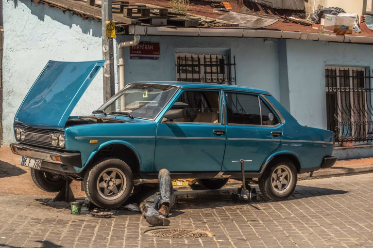 A man lies under a jacked up older car with its hood up.