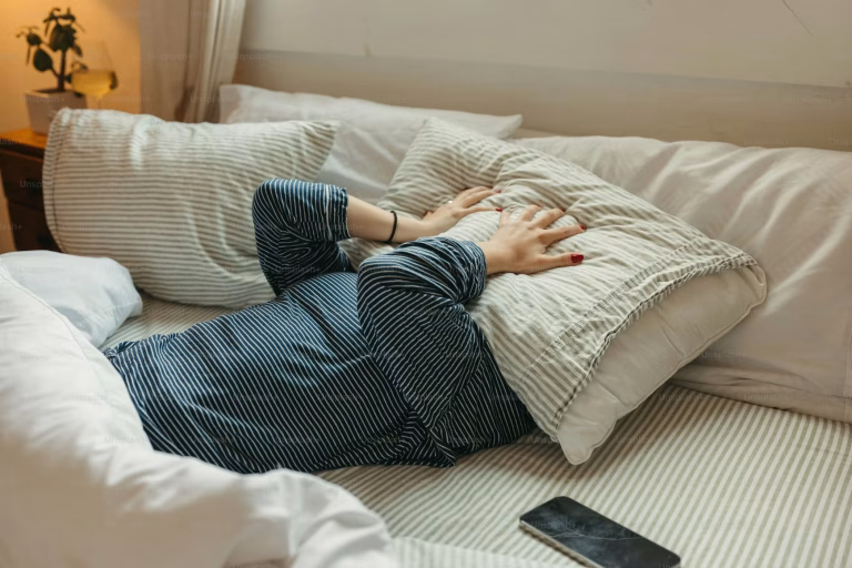 A person lies in bed holding a pillow over their face