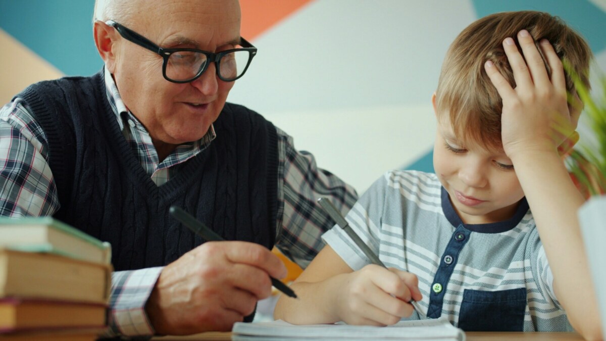 older man with dark glasses and white hair teaches male child with blond hair